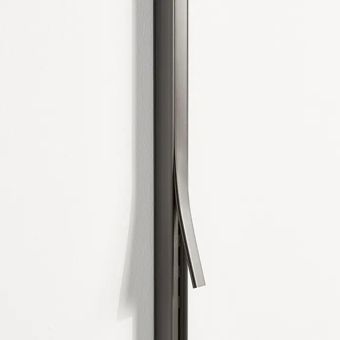 Elfa Garage+/Décor+ by Elfa Abdeckleiste - Höhe: 110 cm, Matt grau - Eine Nahaufnahme eines schlanken, schwarzen Kabelkanals an einer weißen Wand, wobei ein Teil abgelöst ist und das Innere zeigt.