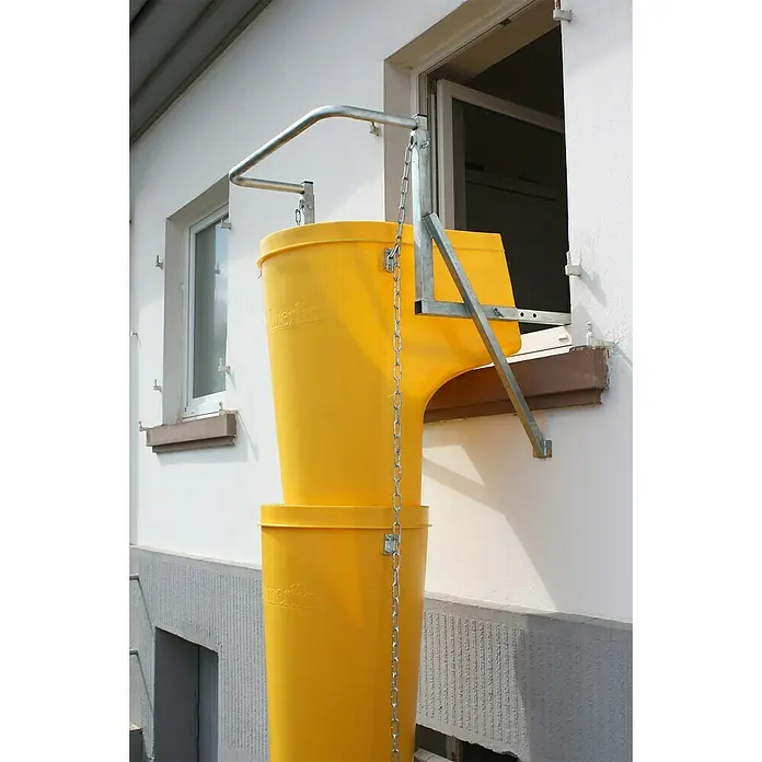 Haemmerlin Schuttrutsche Set 8 - Länge: 8,3 m, Gesamtstückzahl: 8 Stk., Fensterbefestigung - Bauabwurfschacht-System am Gebäude. Das gelbe Kunststoff-System ist mit Metallketten und Halterungen an einem Fenster befestigt für Bauschuttentsorgung.