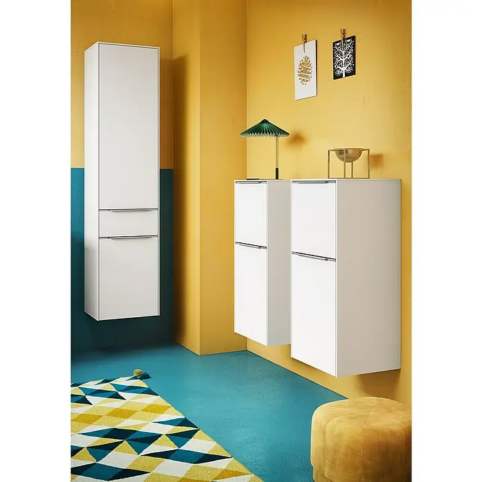 Villeroy & Boch Subway 3.0 Hochschrank - B x T x H: 40 x 36,2 x 171 cm, 1x Schublade, 2x Tür, Pure White, Farbe Griff: Aluminium glänzend, DIN Anschlag: Links - Badezimmer-Interieur mit weißen Hängeschränken an gelben und türkisfarbenen Wänden. Ein gelb-blauer Teppich und ein Hocker ergänzen das moderne Design.