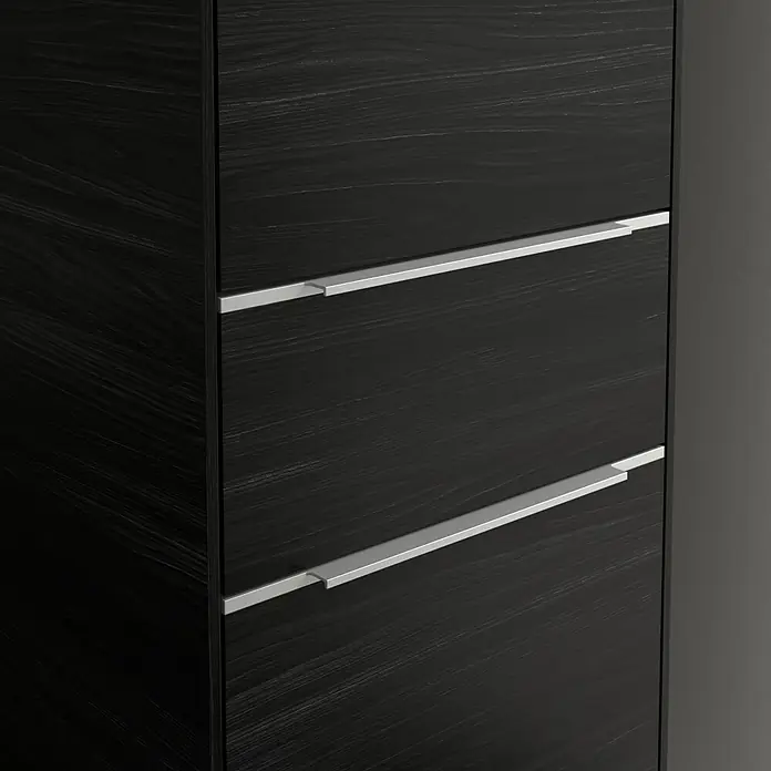 Villeroy & Boch Subway 3.0 Hochschrank - B x T x H: 40 x 36,2 x 171 cm, 1x Schublade, 2x Tür, Black Oak, Farbe Griff: Aluminium glänzend, DIN Anschlag: Rechts - Nahaufnahme einer schwarzen Kommode mit silbernen Griffen. Die Holzmaserung ist deutlich sichtbar und verleiht dem Möbelstück eine edle Note.