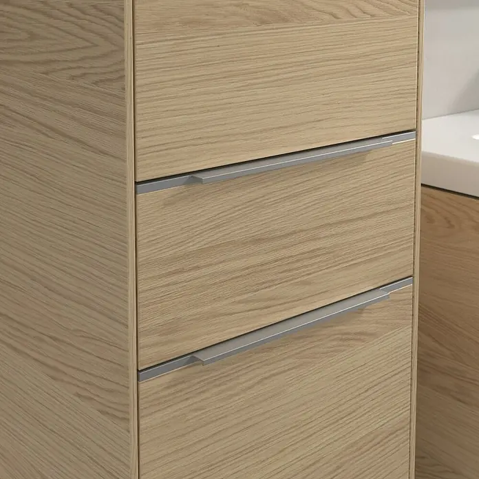 Villeroy & Boch Subway 3.0 Hochschrank - B x T x H: 40 x 36,2 x 171 cm, 1x Schublade, 2x Tür, Nordik oak, Farbe Griff: Aluminium glänzend, DIN Anschlag: Links - Detailaufnahme eines Badezimmerschranks aus hellem Holz mit Schubladen und silberfarbenen Griffen. Der Fokus liegt auf dem Holzdesign.