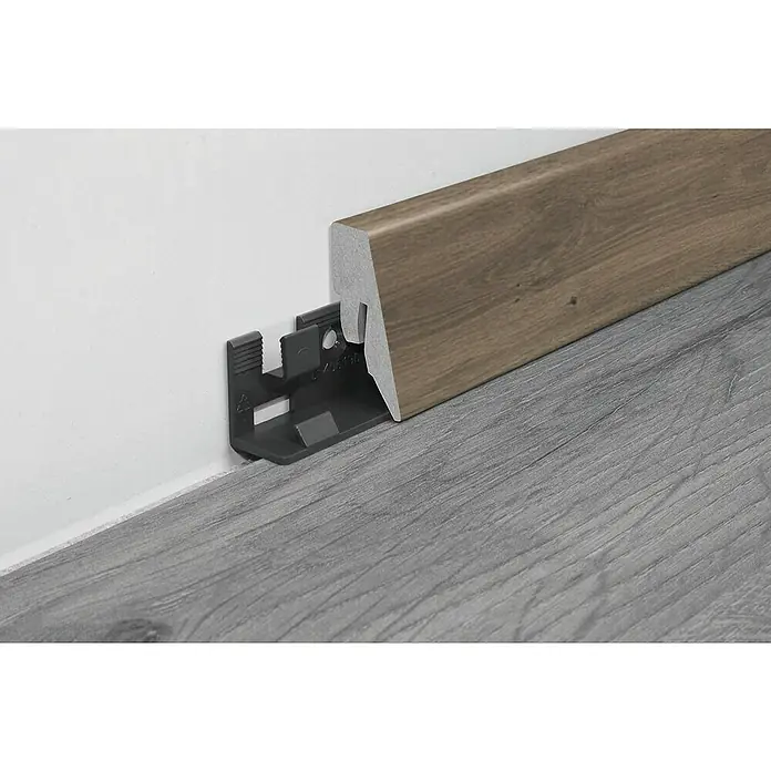 LOGOCLIC Sockelleiste K40 C Eiche Cocoa - 260 x 19 x 40 mm, MDF - Ein braunes Fußleistenprofil mit einem grauen Clip zur Befestigung an einer weißen Wand über einem grauen Boden.