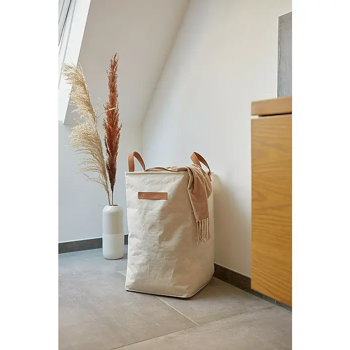 Store It Premium Wäschekorb - L x B x H: 35 x 35 x 58 cm, Beige - Ein Stoffwäschekorb mit Ledergriffen und einem beigefarbenen Schal, der lässig darübergelegt wurde, steht neben einer Vase mit Pampasgras.