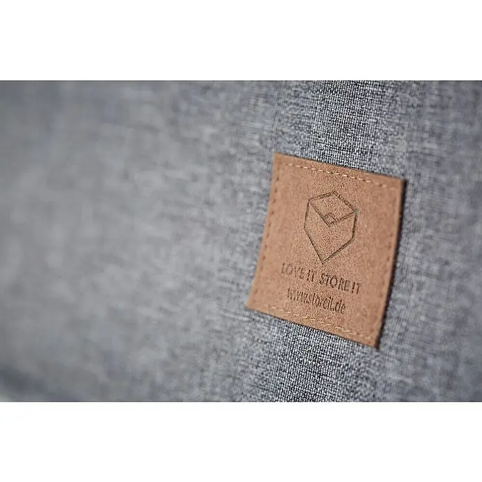 Store It Aufbewahrungsbox mit Klappdeckel - L x B x H: 47 x 30 x 22 cm, Textil, Grau - Nahaufnahme eines grauen Stoffbezugs mit braunem Lederetikett von "LOVE IT STORE IT" mit einer stilisierten Würfelgrafik.
