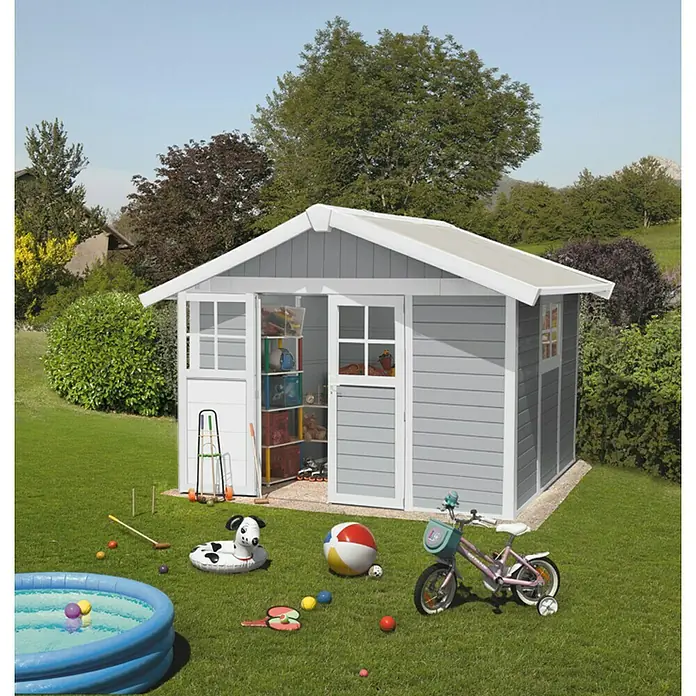 Grosfillex Caseta para jardín Deco - Medidas ext. (An x Pr): 370 x 298 cm, Plástico, Gris claro, 7,5 m² - Una caseta de jardín gris con techo blanco y marcos de ventanas blancos en medio de un jardín lleno de juguetes.