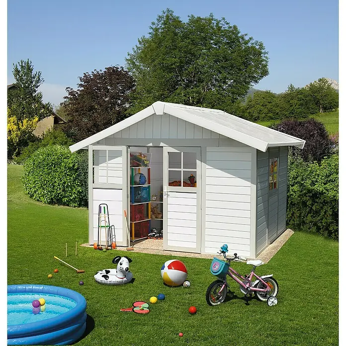 Grosfillex Caseta para jardín Deco - Medidas ext. (An x Pr): 370 x 298 cm, Plástico, Blanco/Gris verdoso, 7,5 m² - Una casita de juegos de madera clara está en un césped verde, rodeada de juguetes y árboles. Esta estructura es ideal para jugar.