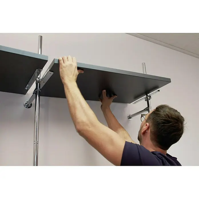 Easy Connect Regalbodenträger - Passend für: Easy Connect Regalsystem, 2 Stk. - Eine Person montiert ein Regalsystem an einer weißen Wand. Das Regal ist dunkelgrau und wird mit Chromstützen befestigt.