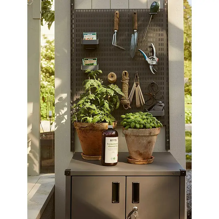 Elfa Garage+ by Elfa Unterschrank - L x B x H: 53,1 x 60,5 x 76,7 cm, Grau matt - Gartenecke mit Rollonda Fermentierter Pflanzennahrung, Werkzeugen und Pflanzen in Töpfen auf einem grauen Schrank.
