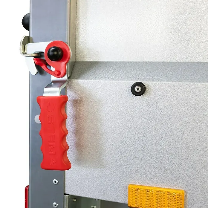 Stema Anhänger BASIC STL 750-21-13 - Nebelschlussleuchte, Nutzlast: 586 kg, Einachser, Kasteninnenmaß: 210 x 128 x 35 cm, Ungebremst - Nahaufnahme eines Stema-Anhängerteils mit rotem Griff und silbernem Mechanismus vor einer grauen Oberfläche.