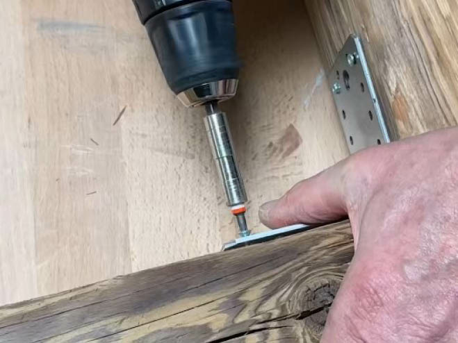 Mit einem Winkelverbinder werden 2 Holzsparren im 90-Grad-Winkel aneinander geschraubt