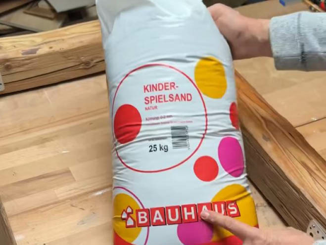 Spielsand wird in die Mitte des Sandkisten-Rahmens gelegt
