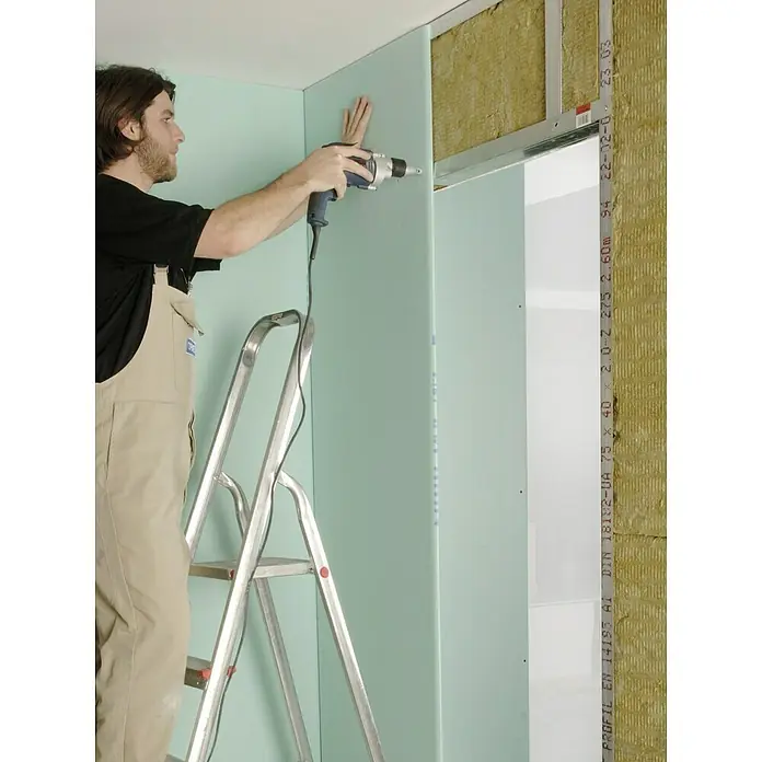 Knauf Schnellbauschraube TN 25 - Durchmesser: 3,5 mm, Länge: 25 mm, 1.000 Stk. - Ein Handwerker befestigt mit einem Akkuschrauber eine grüne Gipskartonplatte an einer Wand, während er auf einer silbernen Leiter steht.