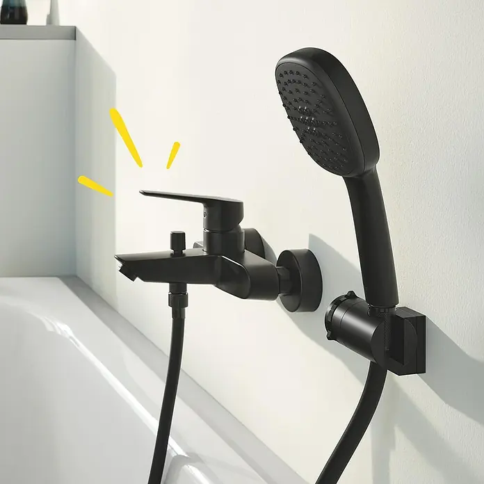 Grohe Start Badewannenarmatur - Ausladung Armatur: 18,8 cm, Schwarz, Matt - Schwarze Badewannenarmatur mit Handbrause an einer weißen Wand montiert, ein elegantes und modernes Badezimmeraccessoire.