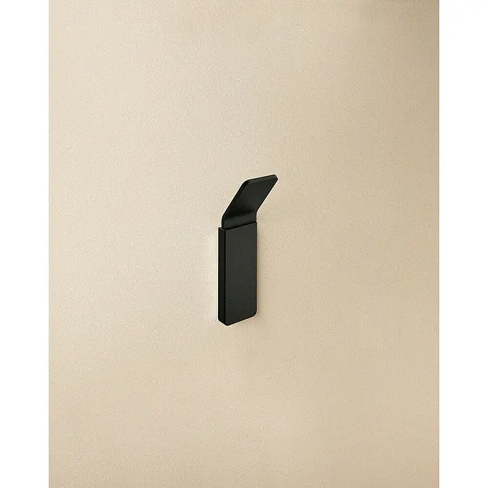 Cosmic Toallero de gancho Nea - 1 ud., Negro, Mate - Un primer plano de un gancho de pared negro moderno montado en una pared beige claro. El gancho presenta un diseño minimalista.