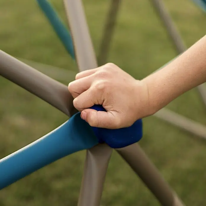 Lifetime Klettergerüst Geodome - 274 x 274 x 137 cm, Metall, Braun, Blau - Nahaufnahme einer Kinderhand, die sich an einem blauen und braunen Klettergerüst festhält, ideal für Spielplätze und aktives Spielen im Freien.