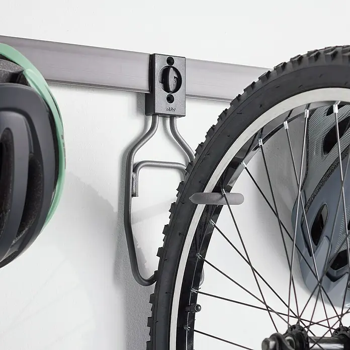 Elfa Garage+ by Elfa Fahrradhaken - L x B x H: 14,3 x 9,8 x 27,5 cm - Nahaufnahme eines Fahrradträgers an einer Wand. Es ist ein System zum Aufhängen eines Fahrrads mit Reifen und einem Fahrradhelm in der Nähe.