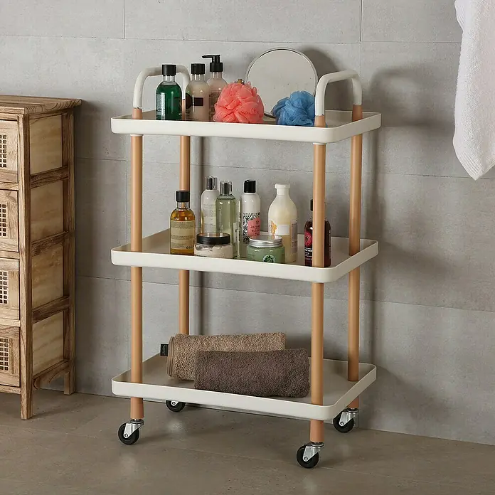 Versa Carro de cocina - L x An x Al: 53,5 x 36 x 85 cm, Blanco - Un carrito rodante de tres niveles con varios artículos de baño, toallas y artículos de tocador contra una pared gris.