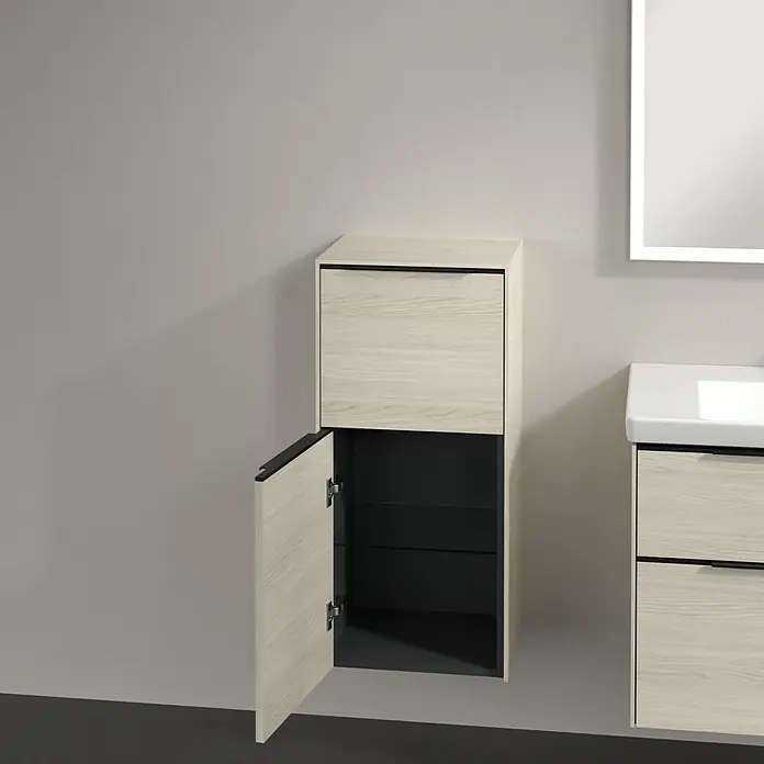 Villeroy & Boch Subway 3.0 Seitenschrank - B x T x H: 40 x 36,2 x 86 cm, White Oak, DIN Anschlag: Links, Farbe Griff: Volcano Black - Der helle Badezimmerschrank mit einer offenen Tür zeigt das dunkle Innere mit Regalen. Daneben befindet sich ein Waschbeckenunterschrank.