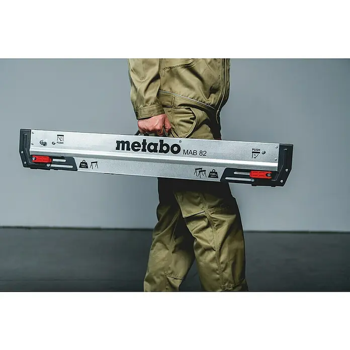 Metabo Arbeitsblock-Set - Stahl, 2 -tlg. - Eine Person trägt einen Metabo MAB 82 Bohrständer. Der Bohrständer ist silberfarben mit schwarzen Akzenten und roten Schiebern.