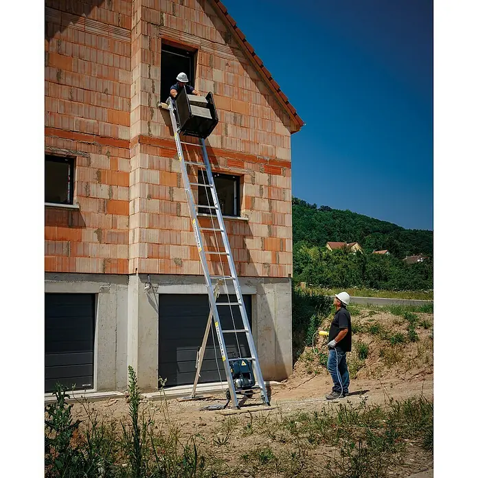 Haemmerlin Maxial Bauaufzug Premium 175/20 Dachdecker - Länge: 10,5 m, Aluminium, Ausführungseigenschaft: Dachdeckerpritsche - Bauarbeiter benutzen einen Bauaufzug, um Materialien in ein Gebäude zu heben. Der Aufzug steht vor einer noch unfertigen Ziegelsteinwand.
