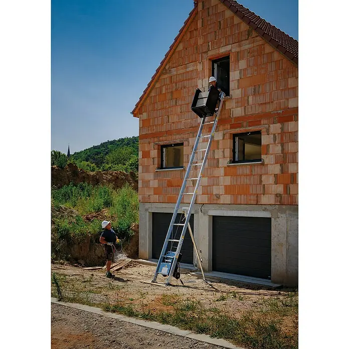 Haemmerlin Maxial Bauaufzug Expert 250/40 Dachdecker - Länge: 10,5 m, Aluminium, Ausführungseigenschaft: Dachdeckerpritsche - Ein Bauarbeiter bedient einen FlexoMobil Aufzug, um Baumaterialien in ein Haus zu transportieren.