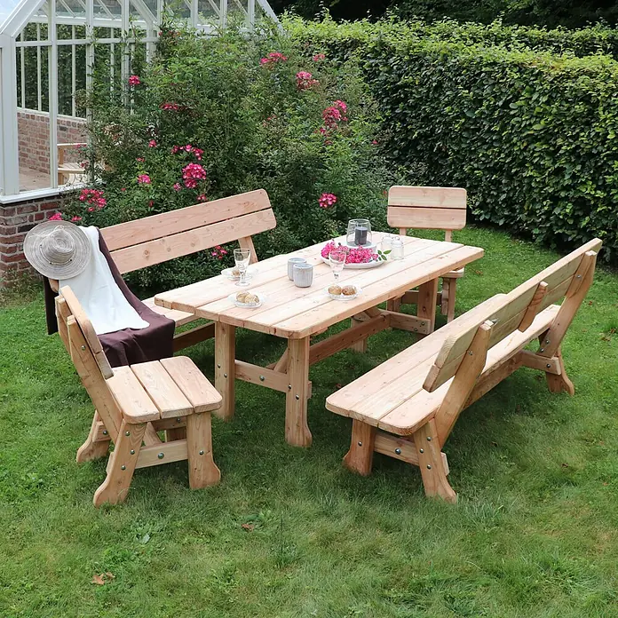 Joda Gartenbank Vogtland - B x T x H: 200 x 43 x 93 cm, Lärche, Natur - Ein hölzernes Gartentisch-Set mit Bänken und Stühlen, ideal für Mahlzeiten im Freien. Das Set ist umgeben von Grün und Blumen.