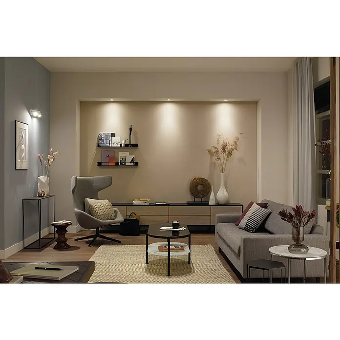 Philips Hue LED-Einbauleuchten-Set rund White Ambience Recessed Milliskin - 4,2 W, Ø x H: 9 x 10 cm, Weiß, 3 Stk., Kaltweiß - Das Bild zeigt ein stilvolles Wohnzimmer mit einem grauen Sofa, einem Sessel und einem Couchtisch auf einem Teppich. Elegante Details und warmes Licht sorgen für Atmosphäre.
