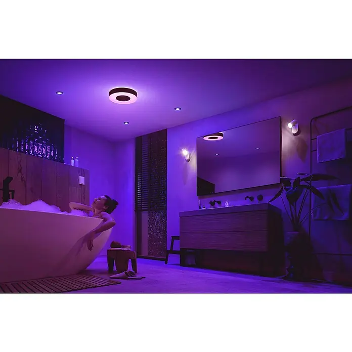 Philips Hue LED-Deckenleuchte rund Xamento - 33 W, Ø x H: 38,1 x 8,4 cm, Schwarz, RGBW - Frau entspannt in Badewanne mit smarten Philips Hue Beleuchtung. Die Deckenleuchte sorgt für stimmungsvolles farbiges Licht im Badezimmer.