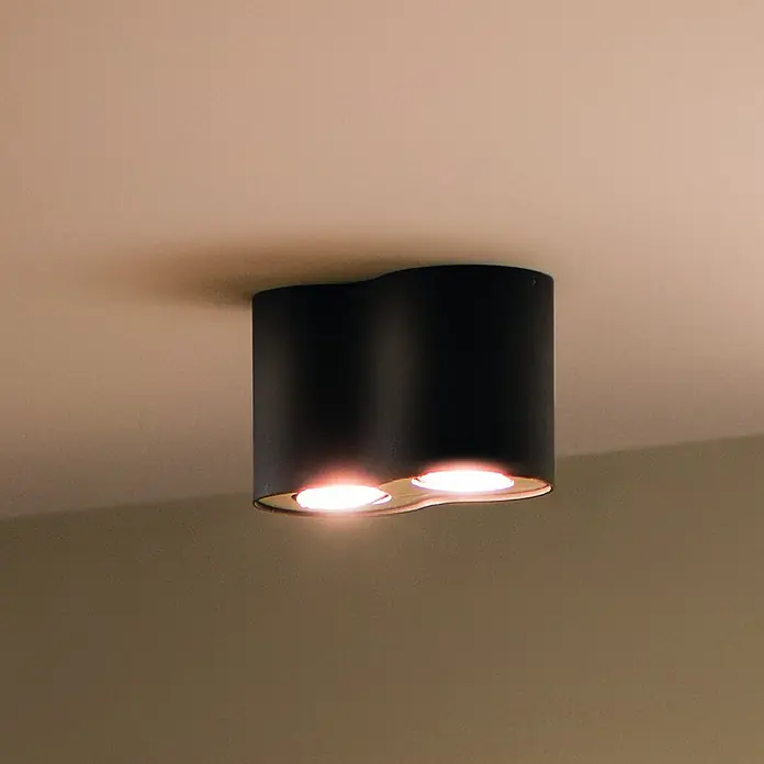 Philips Hue LED-Deckenstrahler White Ambience Pillar - 4,2 W, L x B x H: 19,3 x 10,3 x 12 cm, Weiß, Neutralweiß - Nahaufnahme einer modernen schwarzen Deckenleuchte mit zwei Lichtquellen, die ein warmes Licht ausstrahlen.