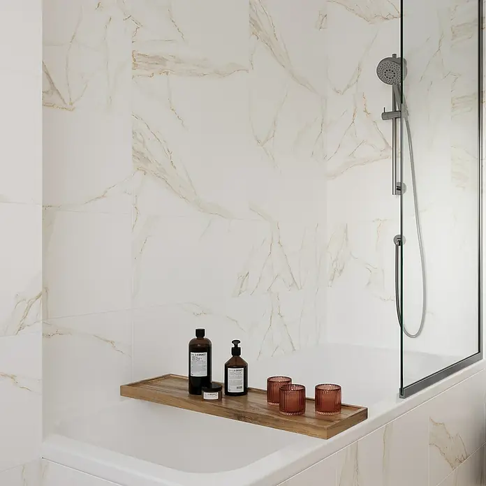 Wandfliese Calacatta - 30 x 60 cm, Weiß/Gold, Glänzend - Badezimmer-Szene mit Badewannenablage mit Hautpflegeprodukten und Kerzenhaltern auf einer weißen Marmorbadewanne mit Duschwand.