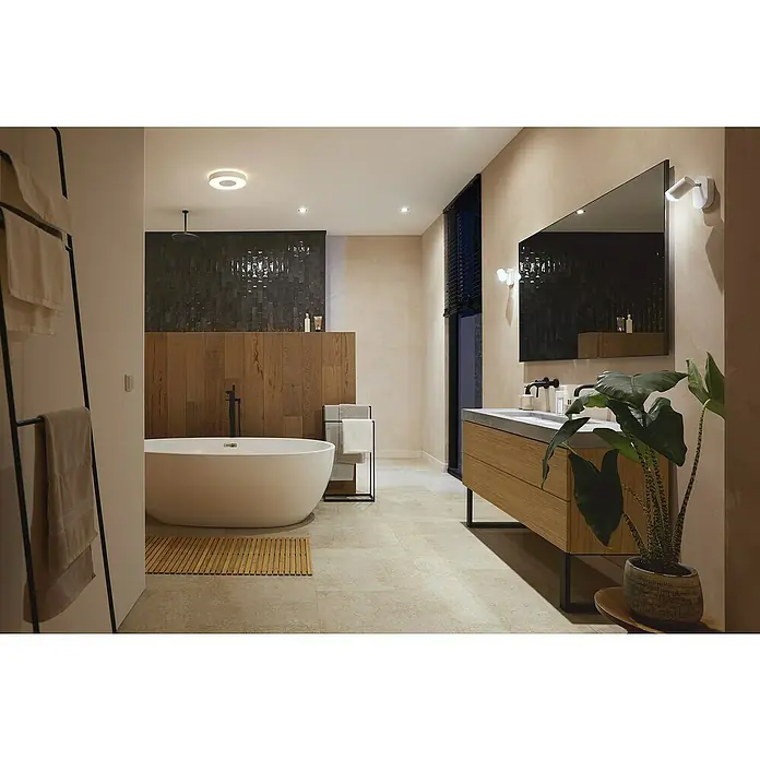 Philips Hue LED-Deckenleuchte rund Xamento - 34 W, Ø x H: 38,1 x 8,4 cm, Weiß, RGBW - Ein elegantes Badezimmer mit einer freistehenden Badewanne, einem Waschtisch aus Holz und einem großen Spiegel, beleuchtet mit modernen Wandleuchten.