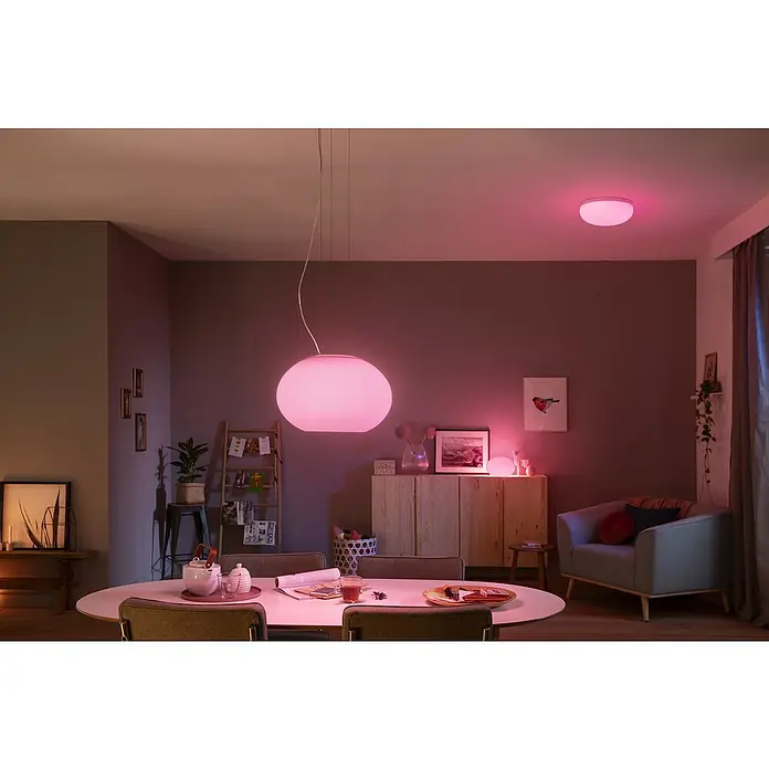 Philips Hue LED-Pendelleuchte Flourish - 39,5 W, L x B x H: 40,1 x 40,1 x 30 cm, Weiß - Das Bild zeigt eine moderne Inneneinrichtung mit einer auffälligen, runden Pendelleuchte, die ein warmes, farbiges Licht ausstrahlt.