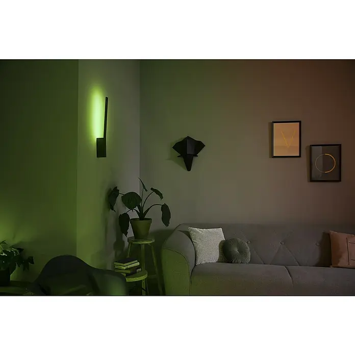 Philips Hue LED-Wandleuchte White and color ambience Liana - 12,2 W, L x B x H: 3,1 x 10,7 x 55,8 cm, Schwarz, RGBW - Elegantes Wohnzimmer mit einer modernen Wandleuchte, die ein stimmungsvolles grünes Licht verbreitet, und einem grauen Sofa mit Kissen.