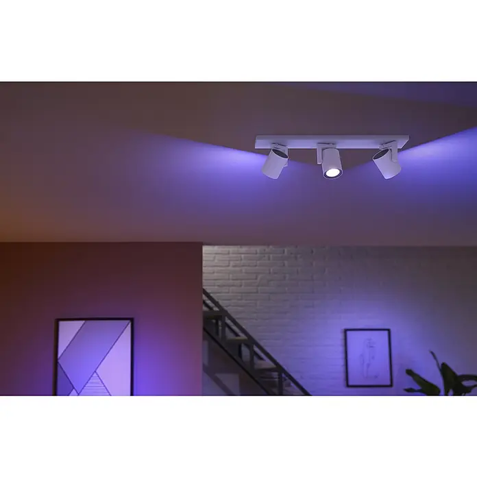 Philips Hue LED-Deckenstrahler White and Color Ambience Argenta - 4,2 W, L x B x H: 48 x 8,9 x 12,6 cm, Weiß, RGBW, Anzahl Leuchtmittel: 3 Stk. - Nahaufnahme einer dreiflammigen weißen Philips Hue Deckenleuchte, die ein stimmungsvolles, farbiges Licht in einem modernen Interieur erzeugt.