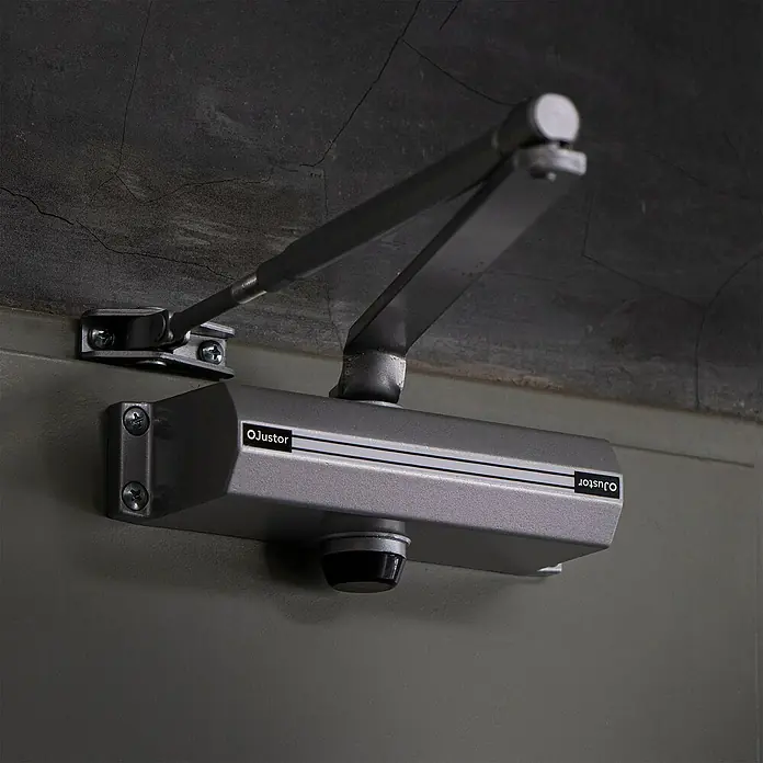 Justor Cerrador de puertas CH - Plateado, Aluminio - Cierrapuertas plateado de Ojustor montado en una puerta, que asegura el cierre automático.