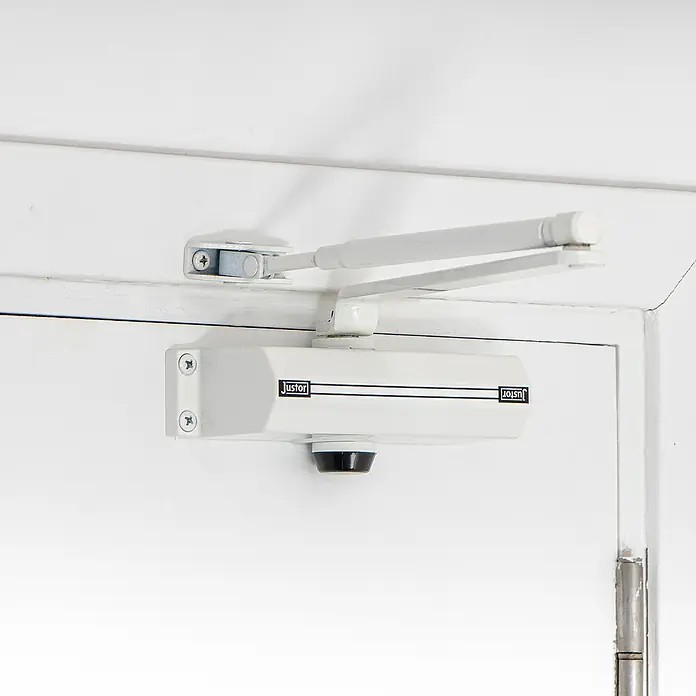 Justor Cerrador de puertas CH - Blanco, Aluminio - Un cierrapuertas blanco Justor montado en una puerta blanca, asegura el cierre automático de las puertas.