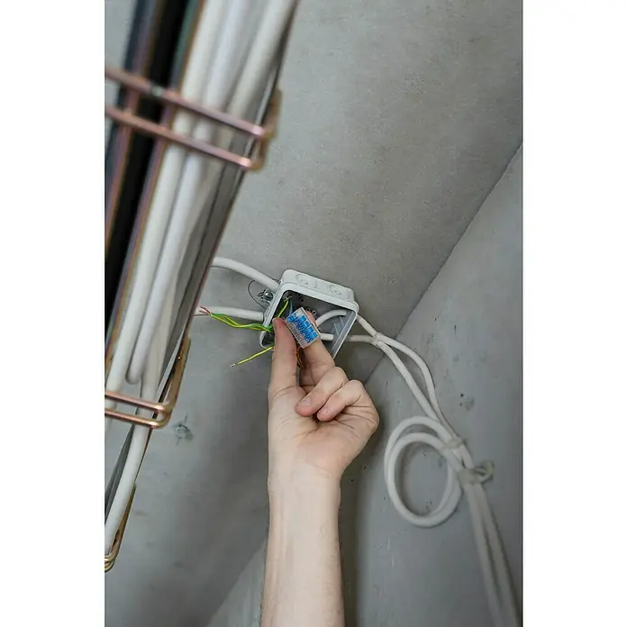 Ideal Hebelklemme Gen II - Anzahl Leiter: 5 Stk., 4 mm², 30 Stk. - Ein Elektriker hält eine blaue Wago-Klemme über einer Abzweigdose mit freiliegenden Drähten, um eine sichere und effiziente Verbindung zu gewährleisten.
