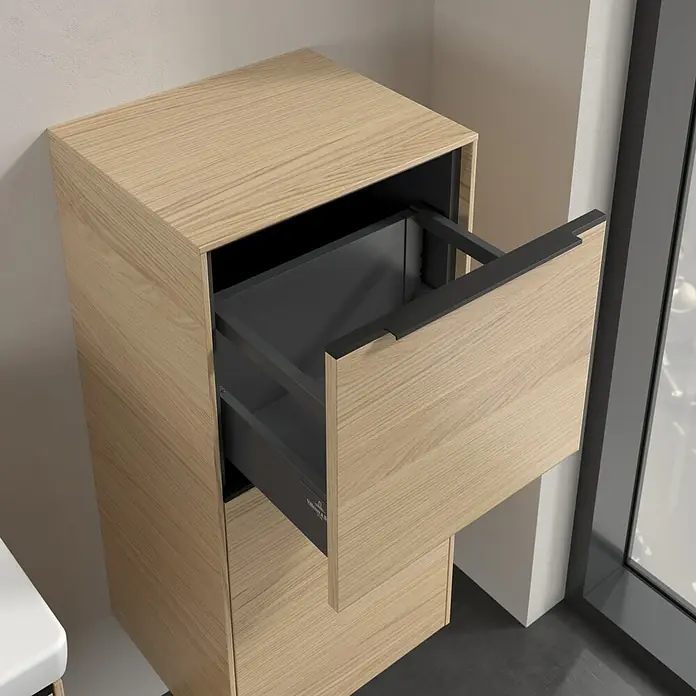 Villeroy & Boch Subway 3.0 Seitenschrank - B x T x H: 40 x 36,2 x 86 cm, Nordik Oak, DIN Anschlag: Rechts, Farbe Griff: Volcano Black - Ein heller Holzschrank mit einer offenen Schublade, die einen grauen Innenraum offenbart, neben einem Fenster für Tageslicht.