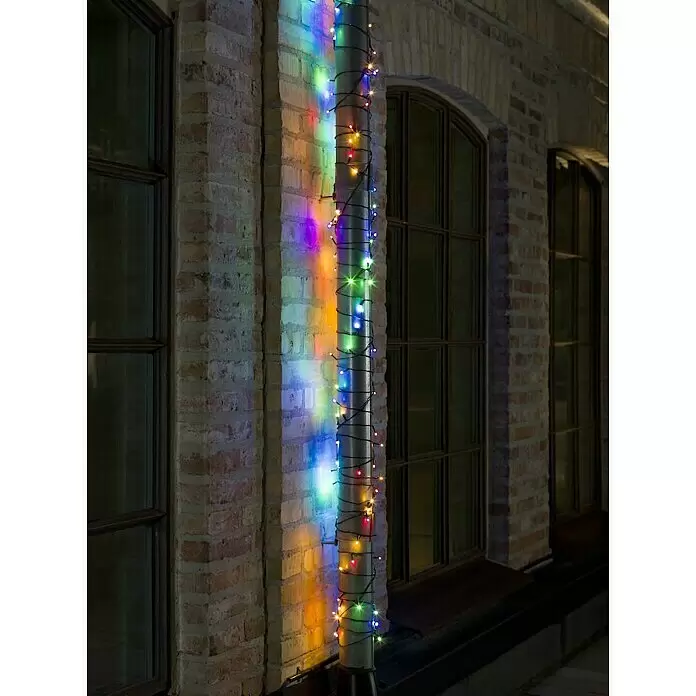 Konstsmide LED-Lichterkette Gefrostet - Außen, Lichtfarbe: RGB, Anzahl Leuchtmittel: 200 Stk., Netzbetrieben, Länge: 41,84 m - Bunte LED-Lichterkette um ein Fallrohr gewickelt, die bunte Reflexionen auf eine Ziegelwand wirft.