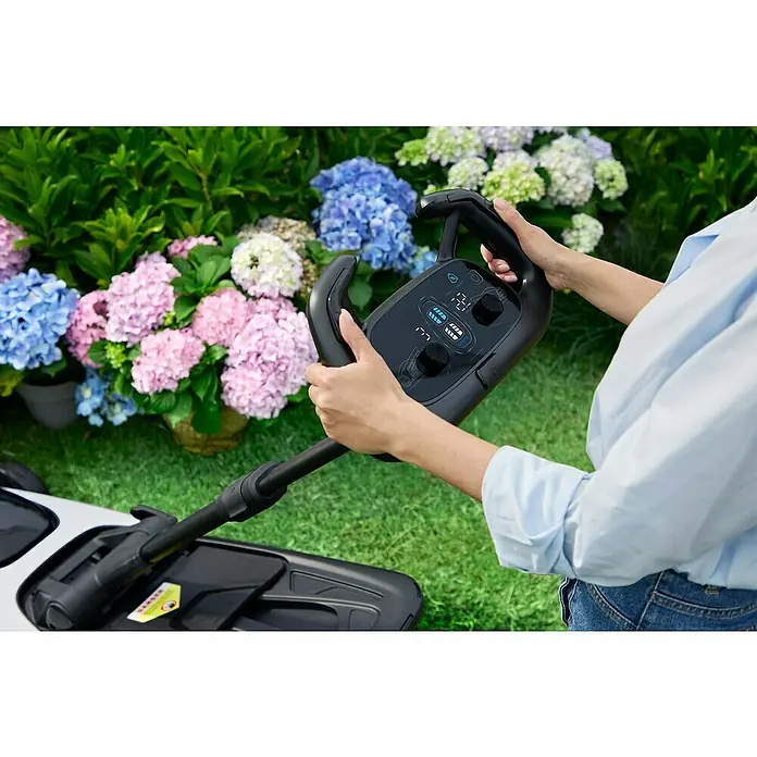 Litheli Akku-Rasenmäher EasySurge - 40 V, 2 Akkus, 4 Ah, Schnittbreite: 43 cm - Nahaufnahme eines Rasenmähers mit Bedienelementen in den Händen einer Person vor einem farbenfrohen Blumenbeet.
