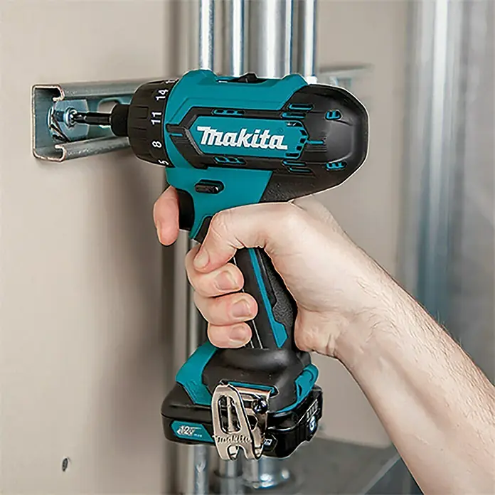 Makita Taladro atornillador percutor de batería DF033DSAE - 12 V, 2 baterías, 2 Ah, 30 Nm - Primer plano de un taladro atornillador inalámbrico Makita que atornilla un tornillo en un perfil metálico.