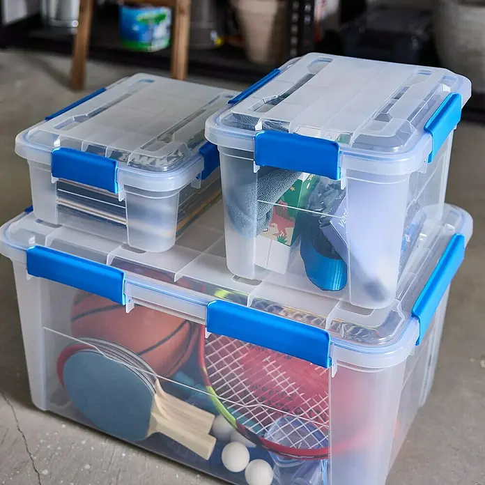Aufbewahrungsbox Wasserdicht - L x B x H: 57,8 x 38,2 x 31,8 cm, Kunststoff, Transparent - Aufbewahrungsboxen aus Kunststoff mit blauen Verschlüssen, gestapelt und mit verschiedenen Gegenständen gefüllt.