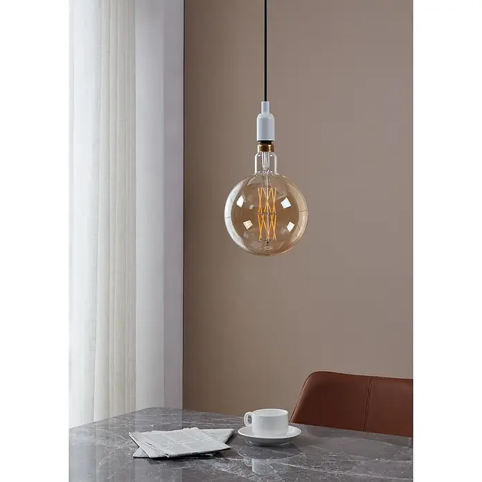 Eglo LED-Lampe - E27, Dimmbar, Warmweiß, 806 lm, 8 W - Nahaufnahme einer großen, runden Glühbirne, die an einem schwarzen Kabel von der Decke hängt, mit einer Kaffeetasse und einer Zeitung auf einem Tisch.