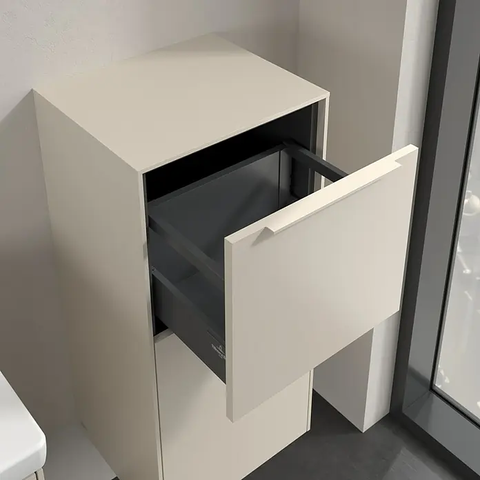 Villeroy & Boch Subway 3.0 Seitenschrank - B x T x H: 40 x 36,2 x 86 cm, Cashmere Grey, DIN Anschlag: Rechts, Farbe Griff: Monochrom - Ein beiger Badezimmerschrank mit einer Schublade, die teilweise geöffnet ist, daneben ein Fenster.