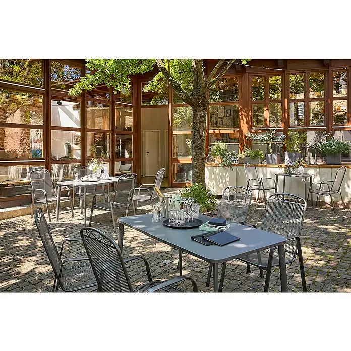 Sunfun Gastro Gartentisch - L x B x H: 142,5 x 82,5 x 75 cm, Stahl, Night-Grey, Stapelbar - Gepflegter Außenbereich eines Restaurants mit Tischen und Stühlen, ideal für Mahlzeiten im Freien.