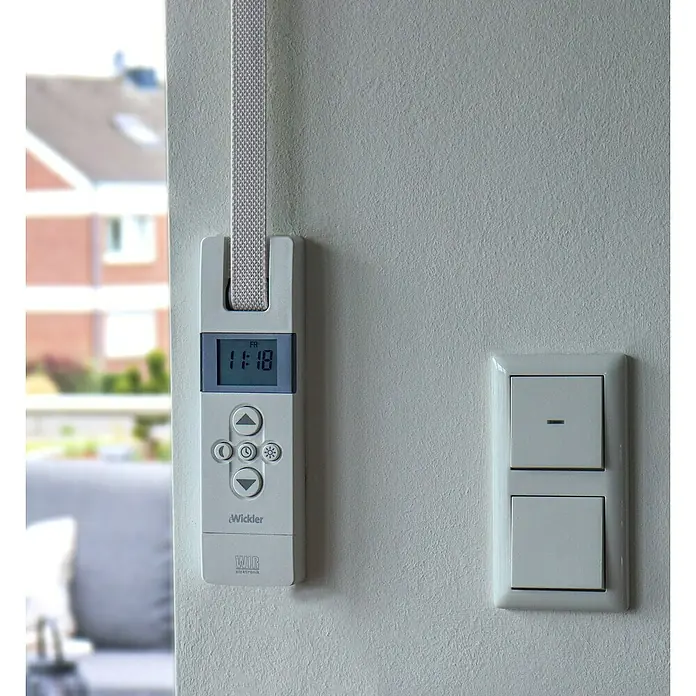 WIR elektronik Rollladen-Gurtwickler Akku EW420-M - Gurtbreite: 12 mm - 15 mm - Nahaufnahme eines Rollladenwicklers mit Zeitanzeige und Bedienelementen, montiert an einer weißen Wand neben einem Lichtschalter.