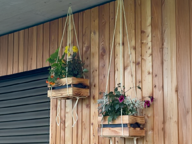 2 fertige Blumenampeln aus Holzkisten hängen auf einem Haken auf der Terrasse