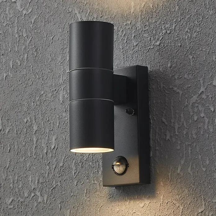 Eglo Außenwandleuchte Riga 5 - 6 W, Schwarz, Anthrazit, Klar, IP44 - Moderne schwarze Wandleuchte mit Bewegungsmelder an einer grauen Wand. Die Lampe ist zylindrisch und strahlt warmes Licht aus.