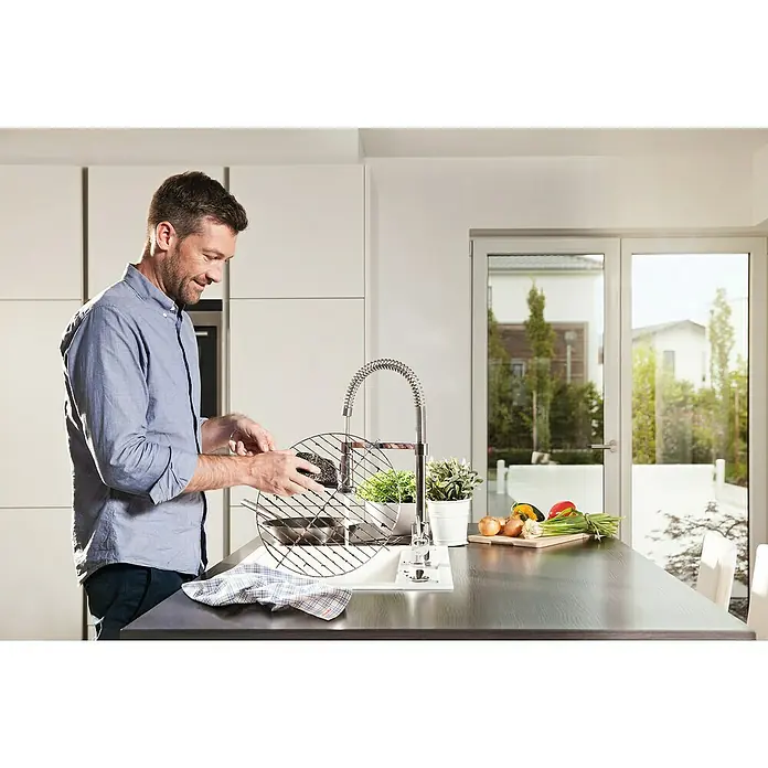 Vileda Glitzi Reinigungspad Power Inox - 2 Stk. - Ein Mann, der in einer hellen Küche einen Grillrost unter einem modernen Wasserhahn spült, mit frischen Zutaten auf der Arbeitsfläche.