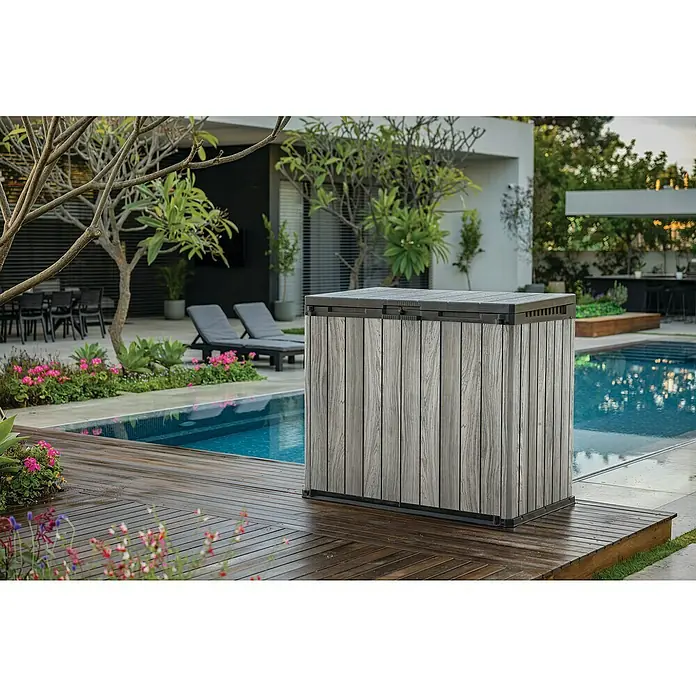 Keter Truhe Store it out Darwin - L x B x H: 80 x 140 x 118 cm, Stormgrey, Kunststoff - Eine graue, holzartige Aufbewahrungsbox steht auf einer Terrasse neben einem Pool. Die Box bietet zusätzlichen Stauraum im Außenbereich.